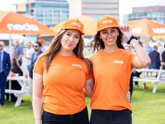 Two women dressed in orange Neds gear pose for a photo