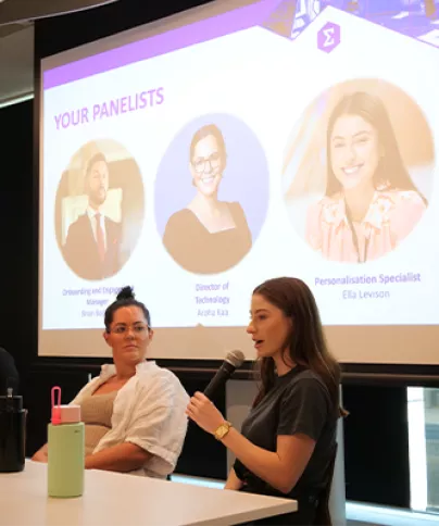 A woman in a panel talks into a microphone during an event