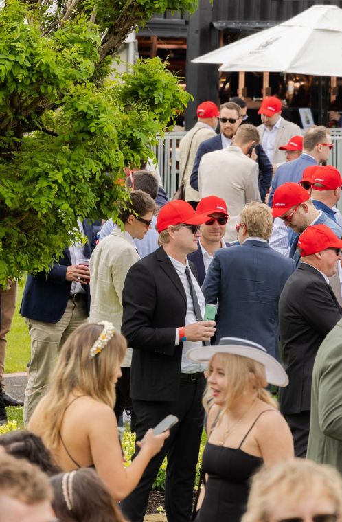 Groups of people wearing red Ladbrokes hats chat at a horse race